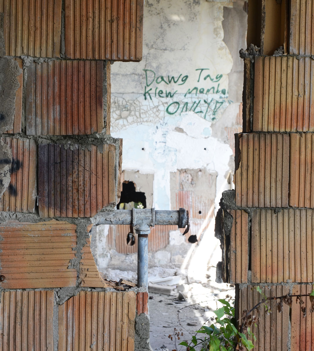 hole in a brick wall, through the hole can be seen graffiti writing on the wall that says Dawg tag klew memba only!