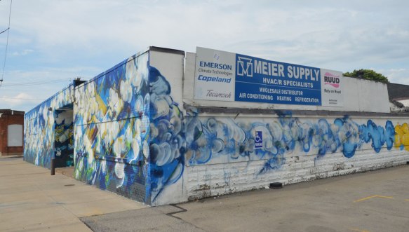 The corner of a one storey building that is covered in a blue and white bubbly looking mural. With a sign for Meier Supply, HVAC Specialists. 