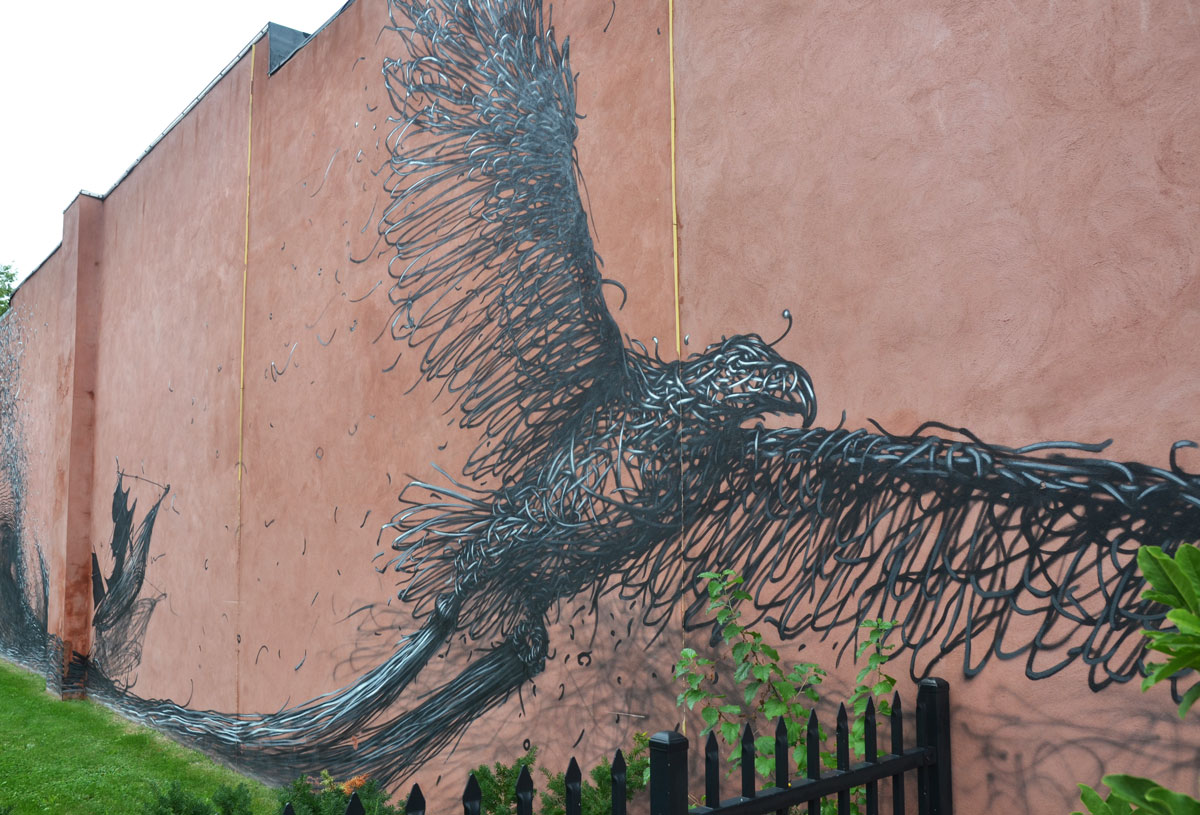 A bird in flight, street art mural, black on red brick. 