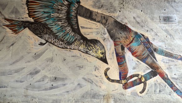 Detail of a large mural. This picture shows a bird in flight swooping down to catch a worm that is being held by the fingers of a hand. 