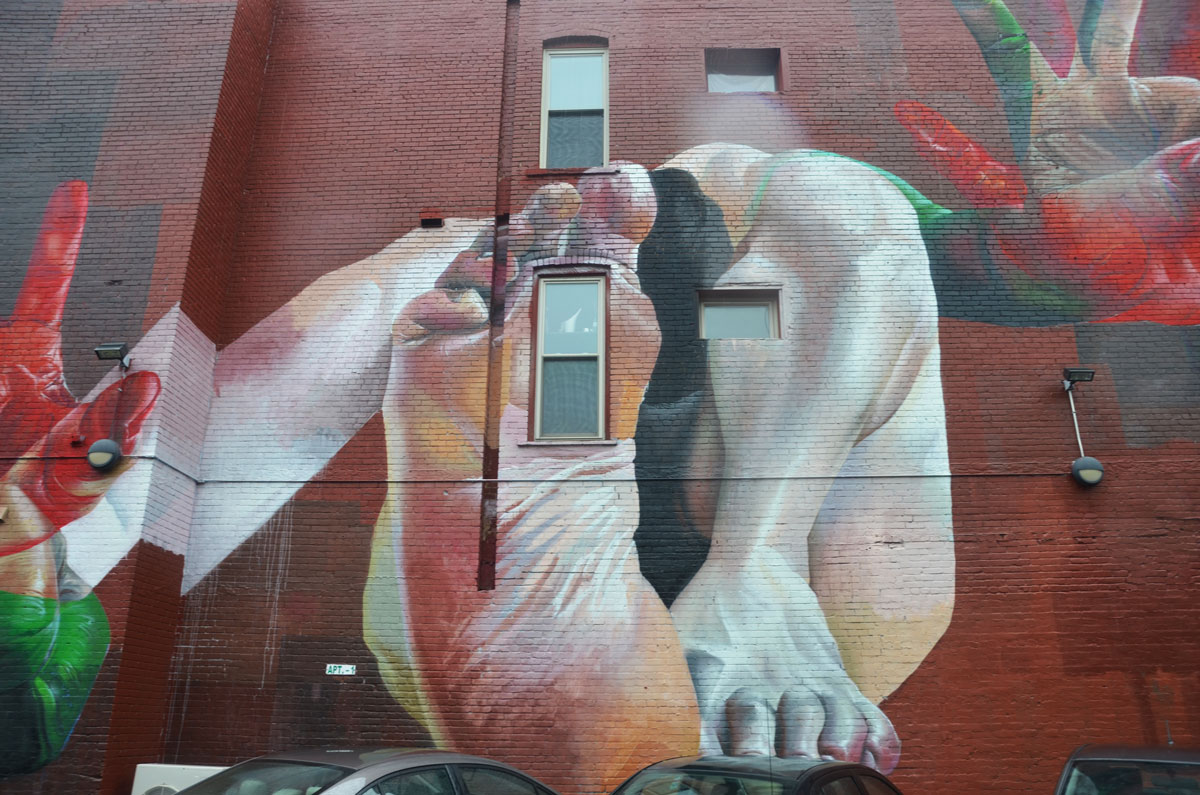 Detail of a larger mural. Showing two feet - one where the bottom of the foot is seen, and the other where the calf and toes are seen. 
