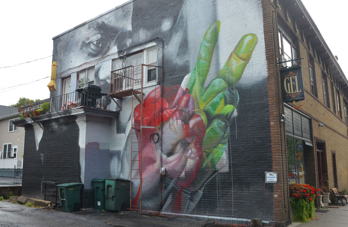 Mural of Martin Luther King on the back of a building. The building has a balcony on which is a barbecue and some chairs. In the mural, his hands are coloured, one in greens and one in reds. 