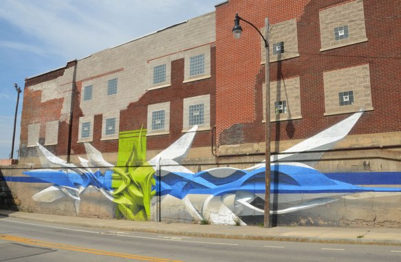 street art art mural on the side of an embankment wall and lower part of a red brick building on Atlantic Ave in Rochester New York