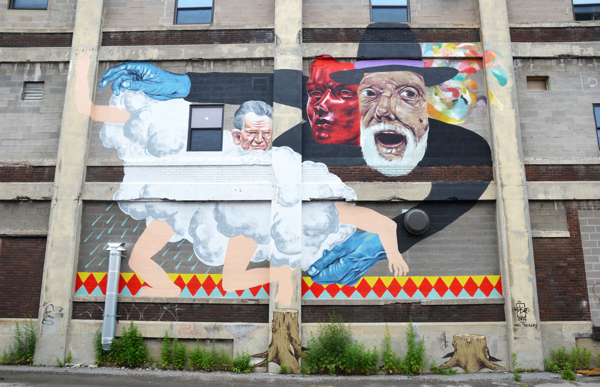 very large mural on the side of a building, three men and a cloud. One man has blue hands. 