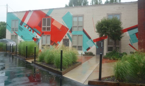 A low building has been painted grey and then rectangular shapes in red and turquoise have been painted on top of that. 