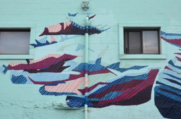 very large street art hand, part of a mural, in blues and purples on a turquoise wall
