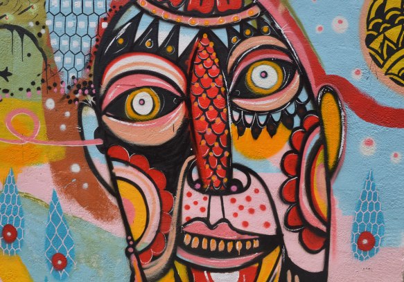 detail of one of the faces in a colourful mural of abstract figues, faces, birds, and fish on the side of a building, There is one word written on mural and it is "understand"