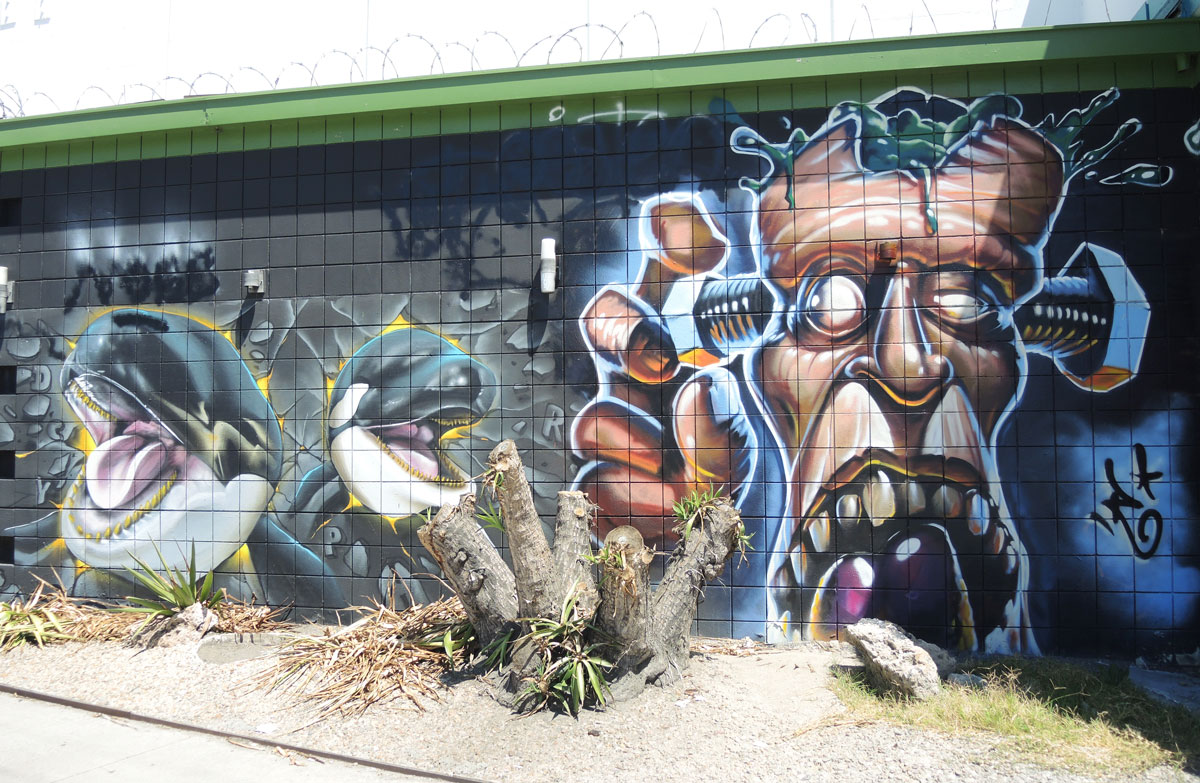 street art painting of two whales on the left side of the picture and a man with large screws on the sides of his head on the right side of the picture. 