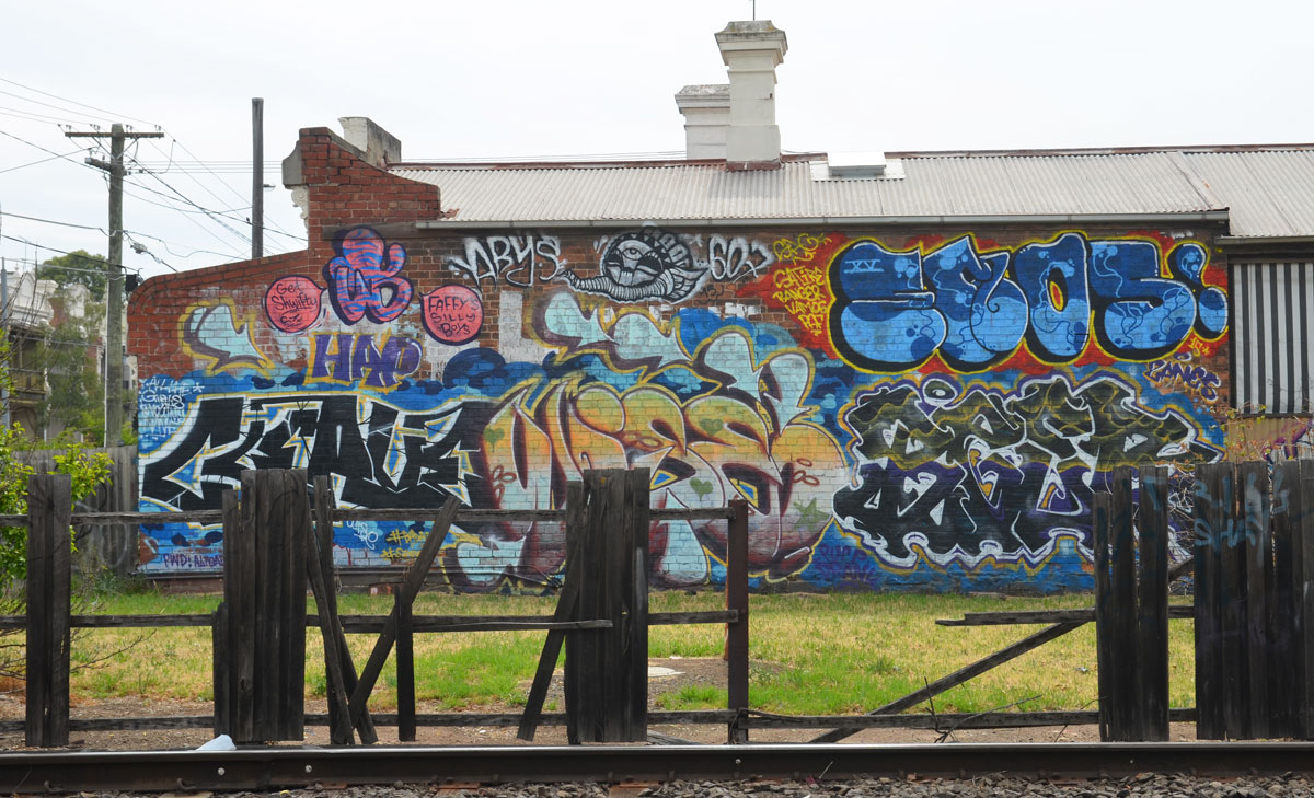 looking across the train tracks to a side of a building that has been covered with street art