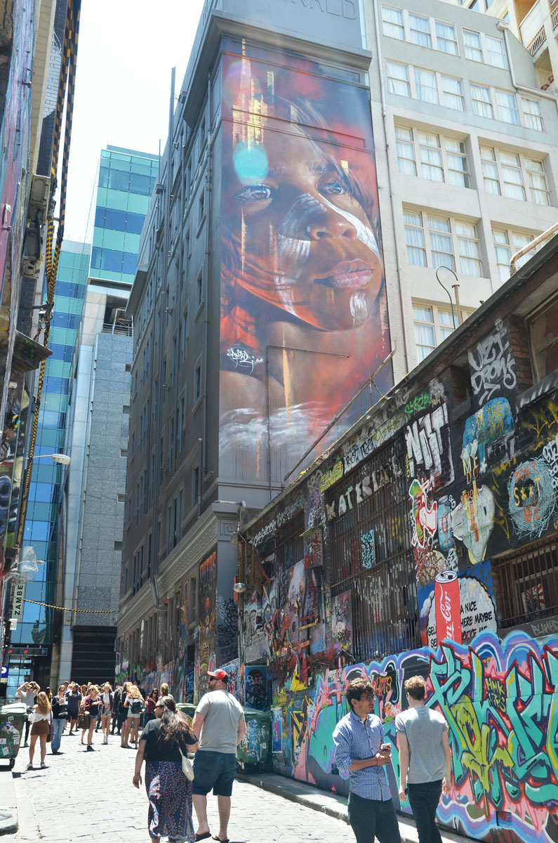 Large mural of the face of an Australian aboriginal boy painted by Adnate in Melbourne - high on a wall overlooking Hosier Lane and all it's graffiti and tourists. 