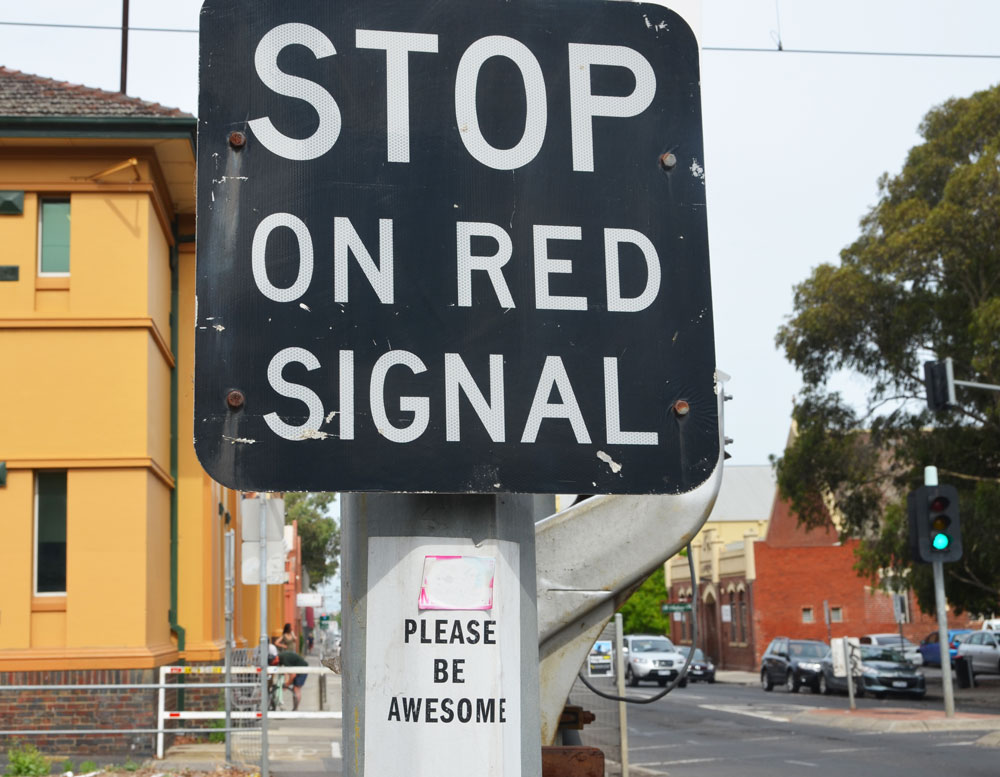 sign at a railway crossing that says Stop on Red Signal. below it someone has posted a sign that says Please be awesome. 