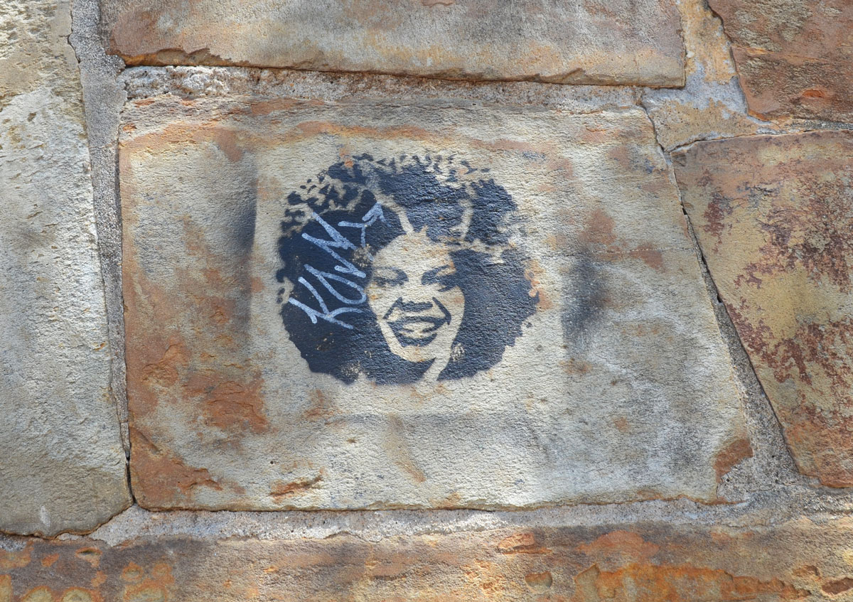 black stencil on a stone wall of a woman's head, very large Afro hair style, smiling, 