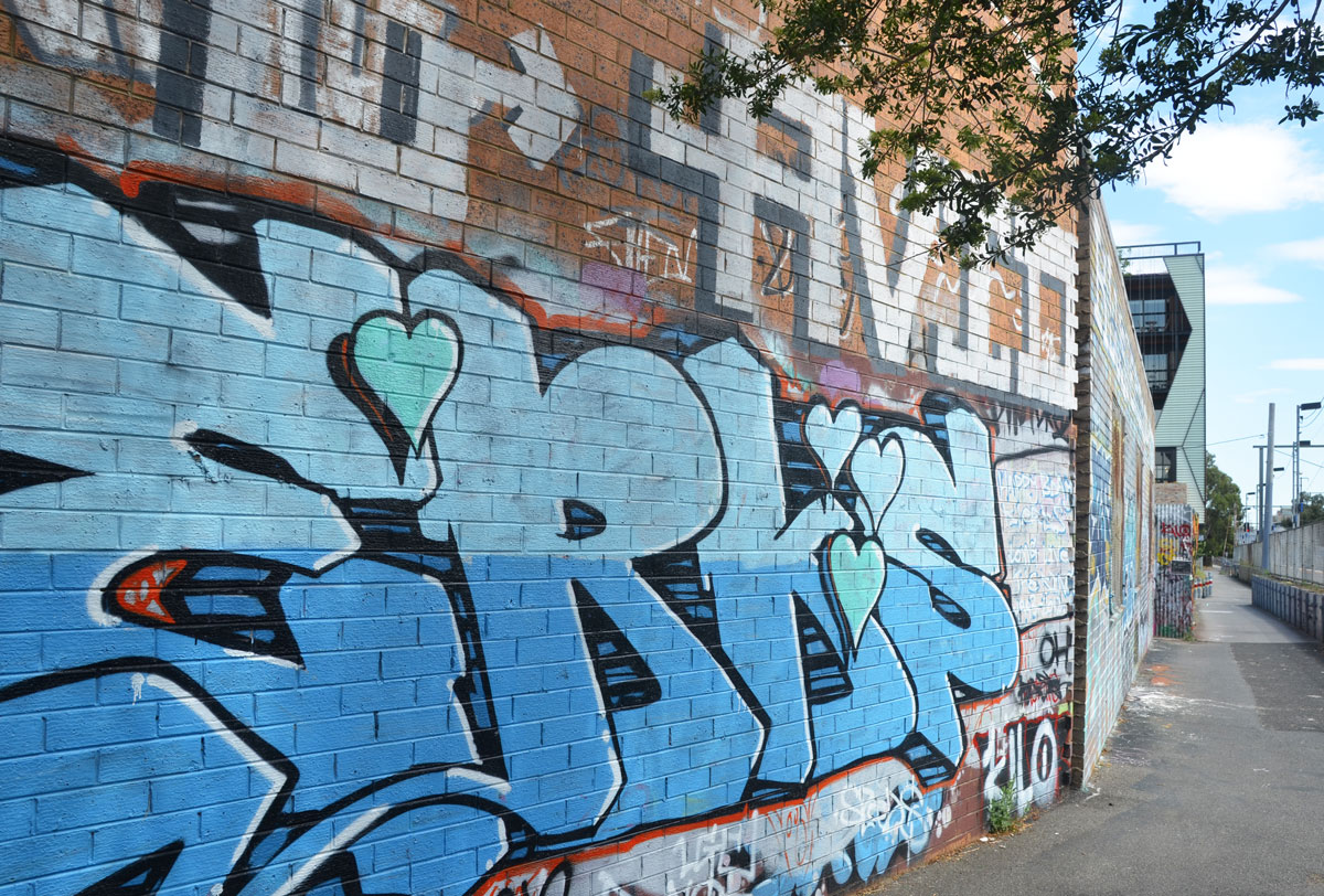 wall beside a bike path and train track, with a blue tag that includes 4 hearts