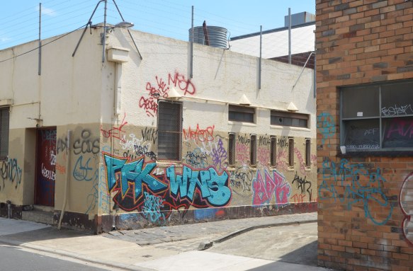 The corner of a one story white building that has a lot of graffiti on the lower half of the building. 