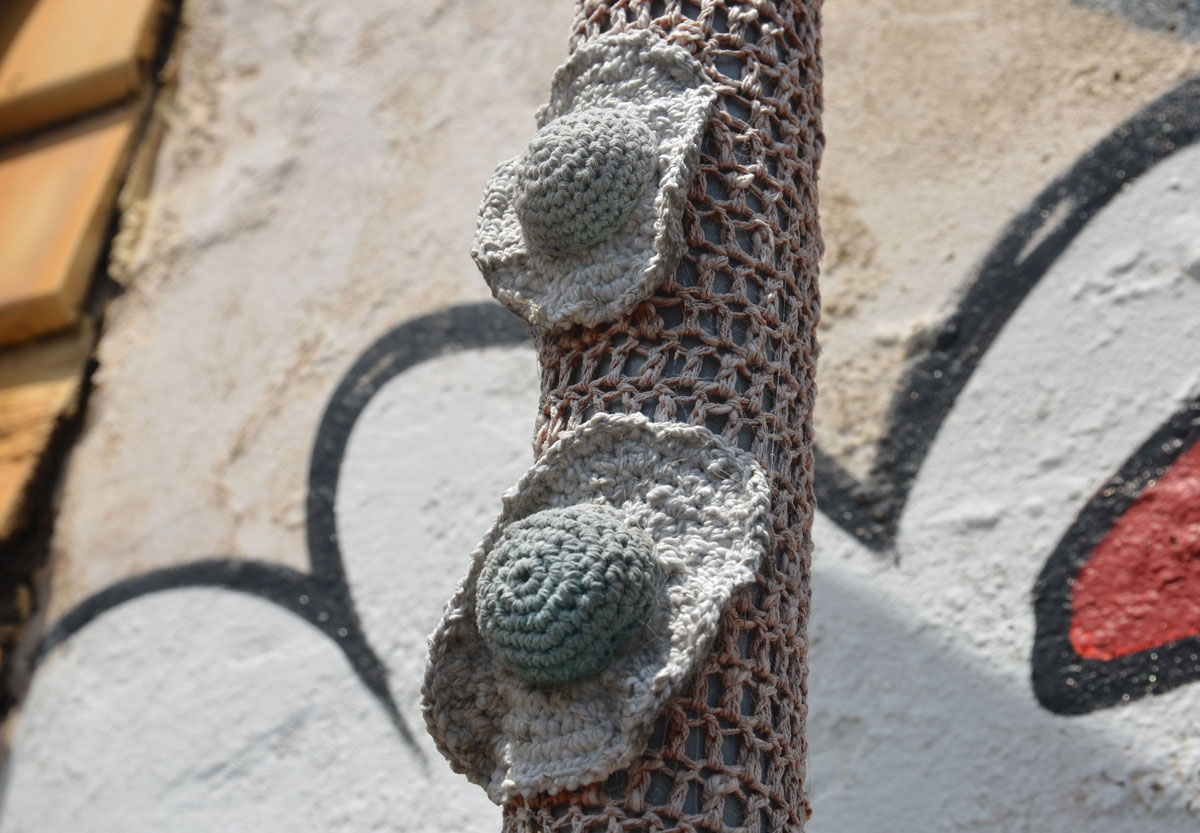 Two little grey crocheted sun hat shapes attached to a pole that is covered in beige crochet. 