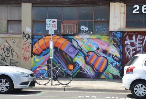 mujlti coloured mural that includes an orange and purple guitar. A bike is parked in front of the mural 