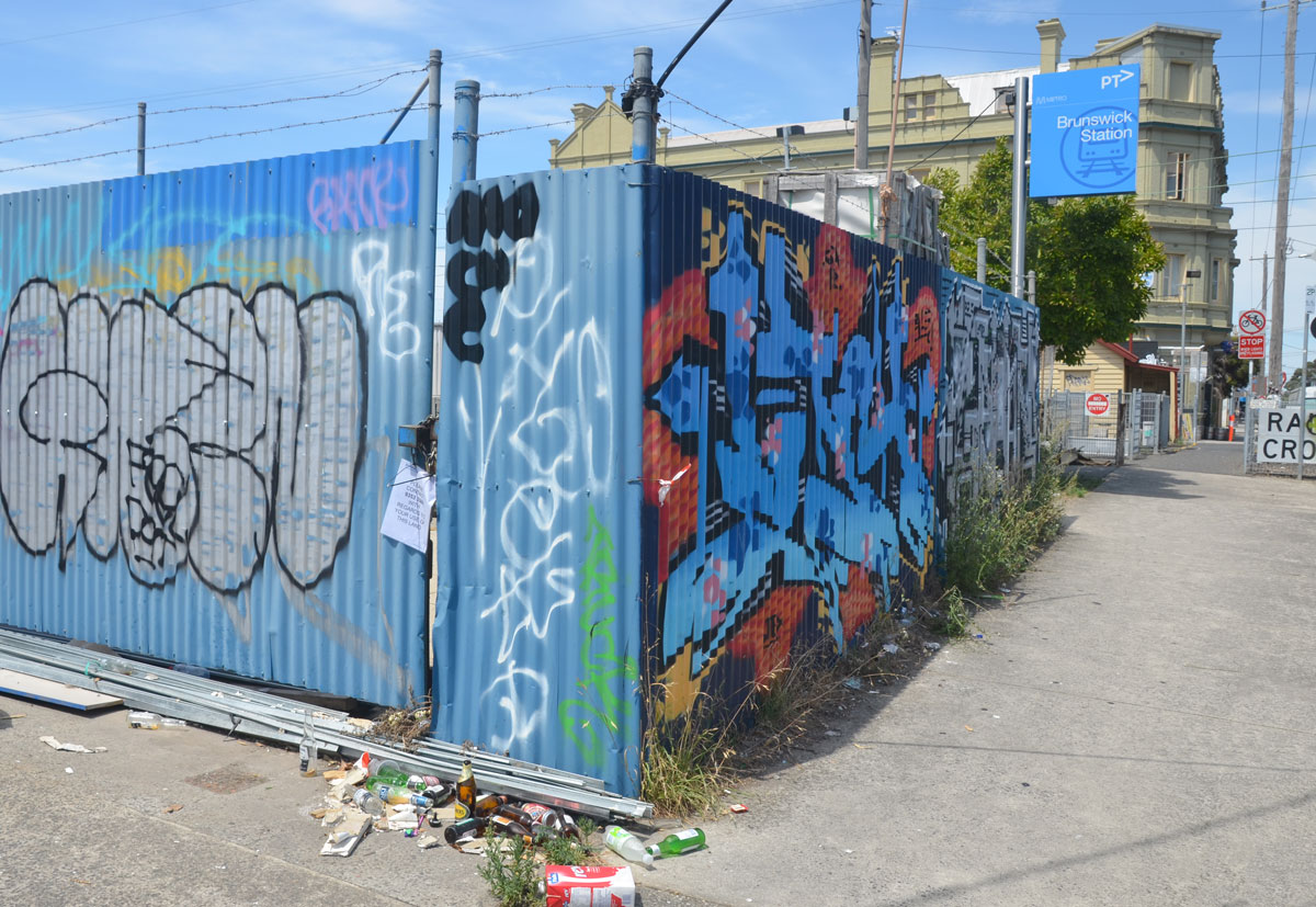 Graffiti on a corrugated metal fence. The Railway Hotel is in the background. 
