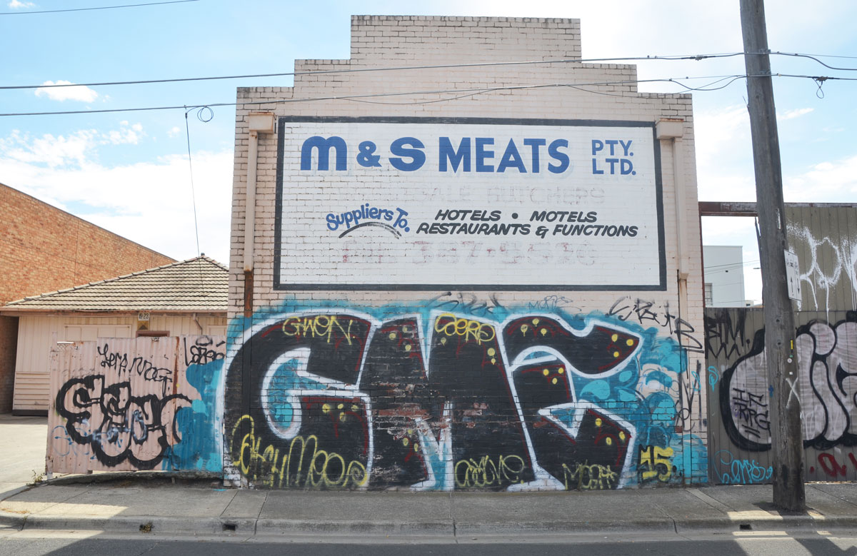 Graffiti on the lower level of M & M Meats pty ltd. C M E in large black letters on a blue background. 