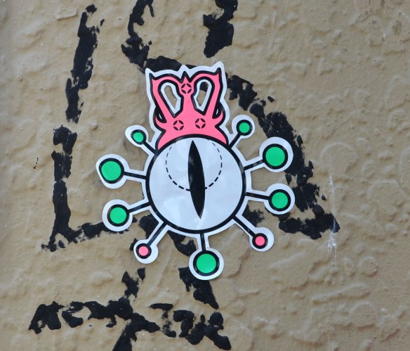 A sticker on a grey wall. White circle with green dots around it, a little pink blob creature sitting on top of it