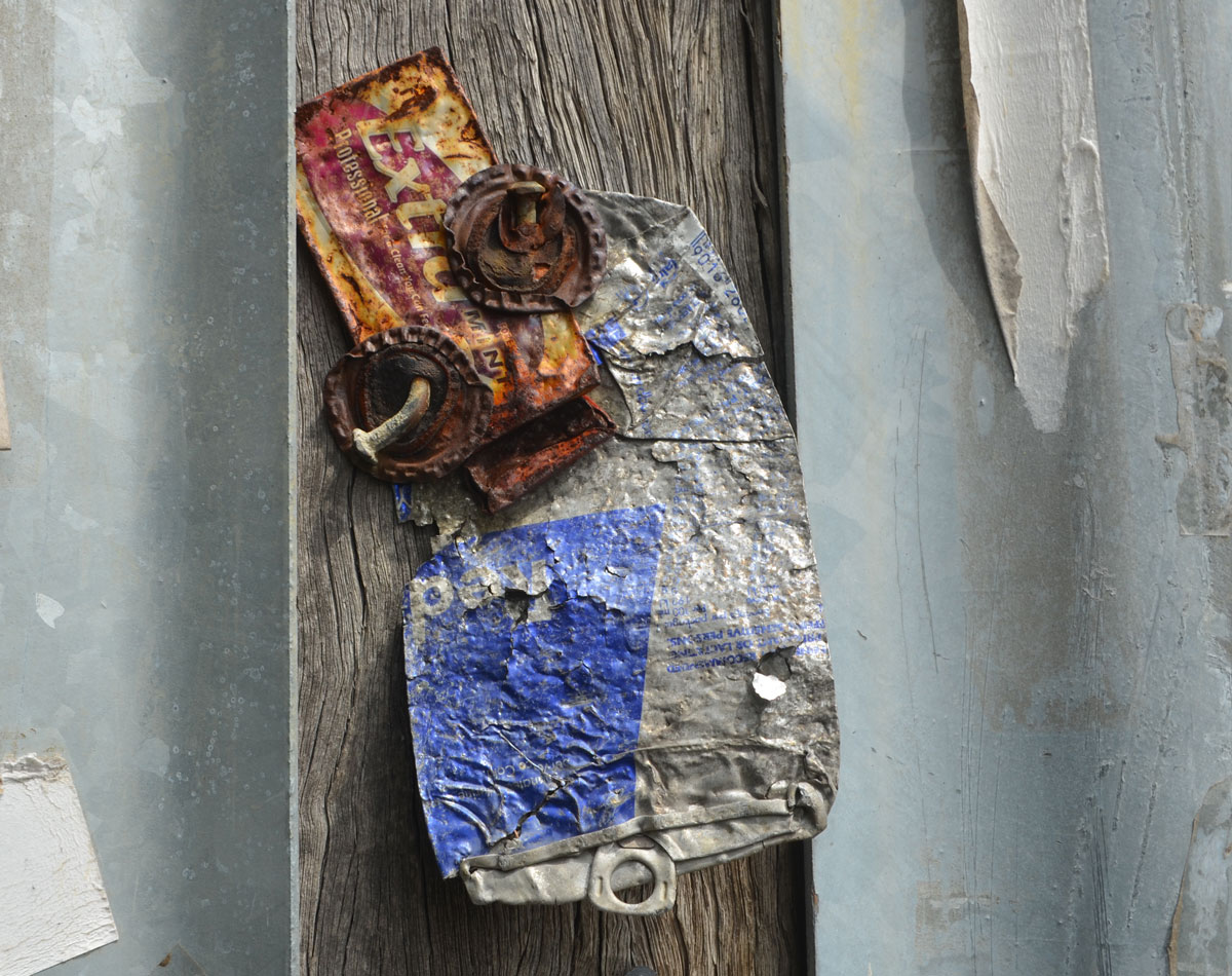 nailed to a wooden telephone pole is a little creature made from a flattened pop can, another metal label and two bottle caps for eyes. 