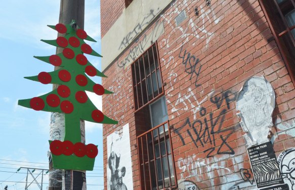 A green cutout in the shape of a Christmas tree attached high up on a telephone pole. red circles are attached to it to look like tree ornaments.