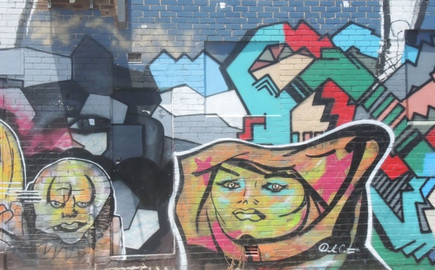 part of a larger mural in an alley, two faces in bright colours,