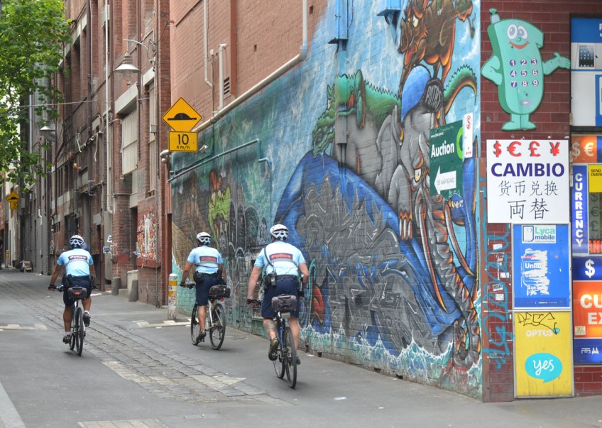 Three policemen on bikes ride down a lane past a street art mural