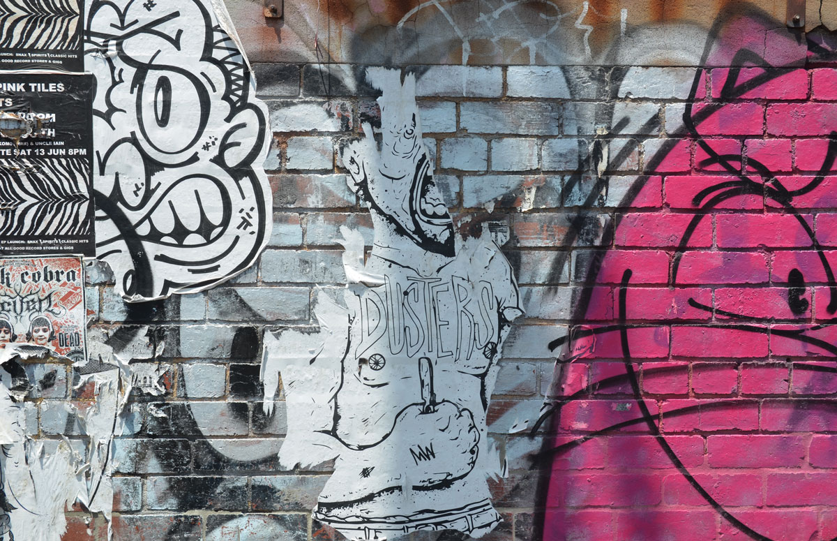 torn wheatpaste street art of a bare chested man, arm bent at the elbow, holding something in his hand. He is yelling but half of his face is missing 