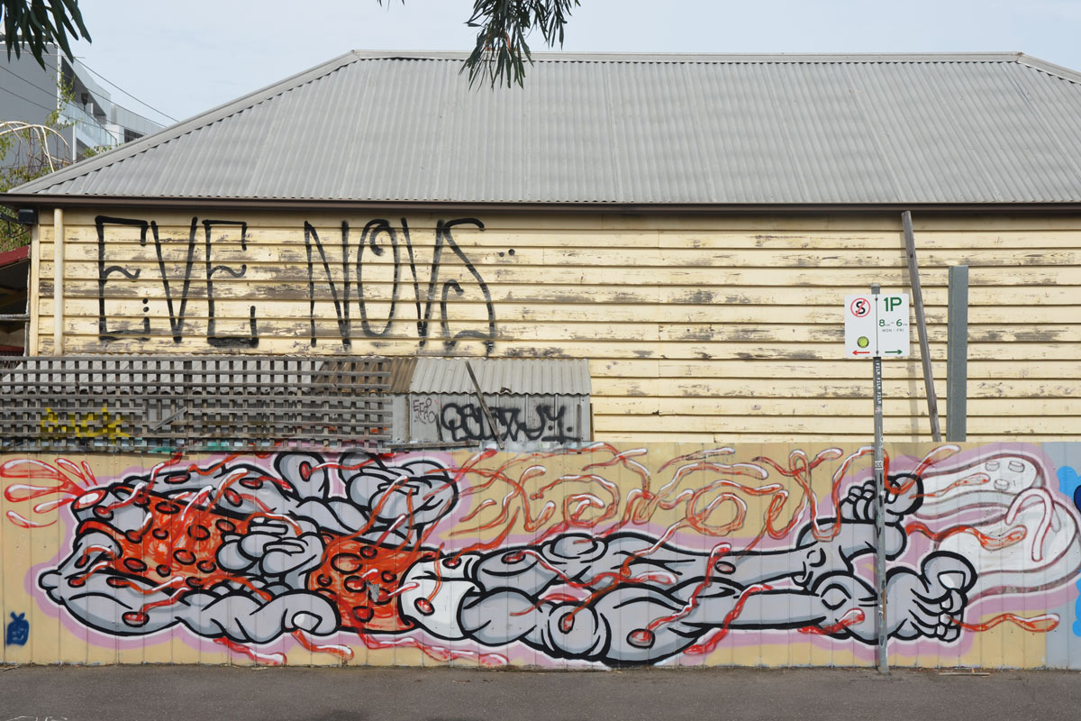 long abstract looking headless man lying horizontal, street art painting across the bottom of a building with wood siding. Written above in large black letters is Eve Novs