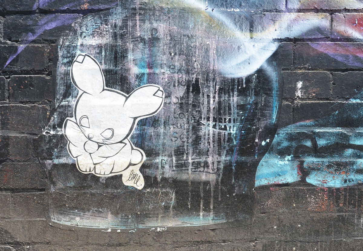 a wheatpaste bunny, white with black outline on a wall with a faded outline of a head in profile, otherwise painted black and blue
