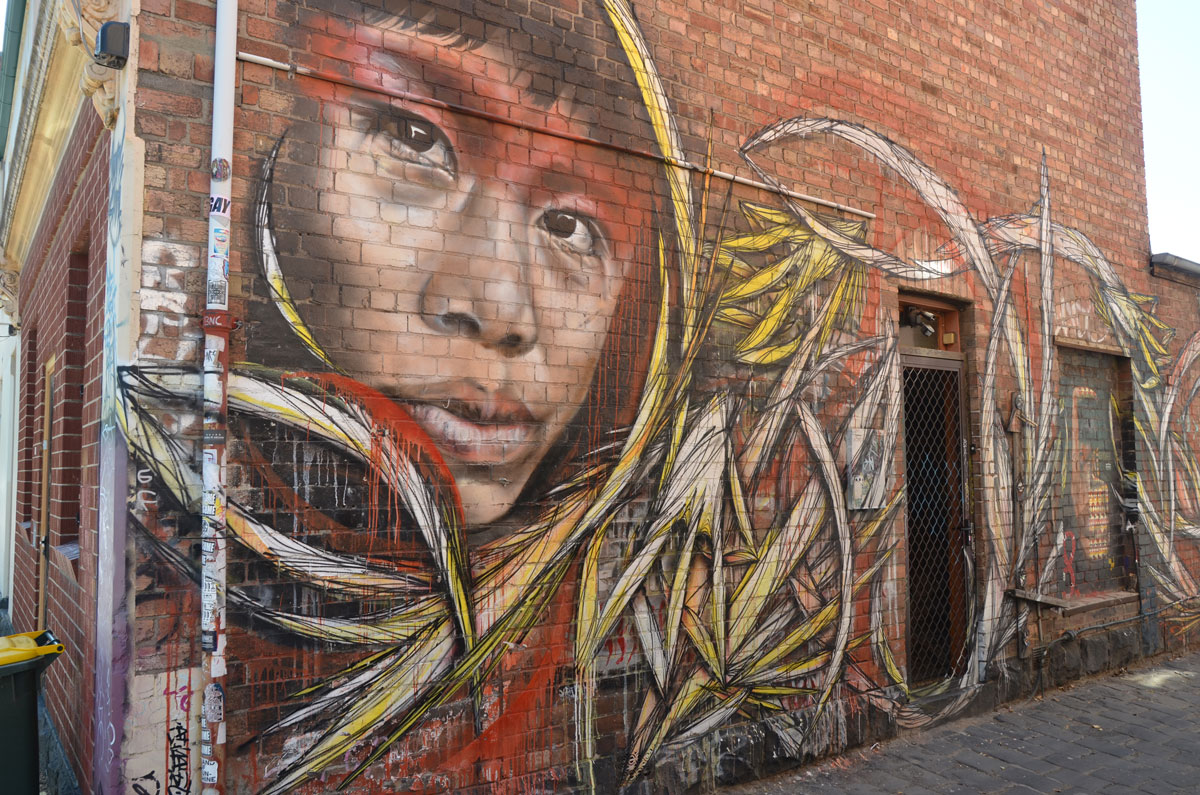 in an alley, mural of a person's face, looking over his/her shoulder at the street