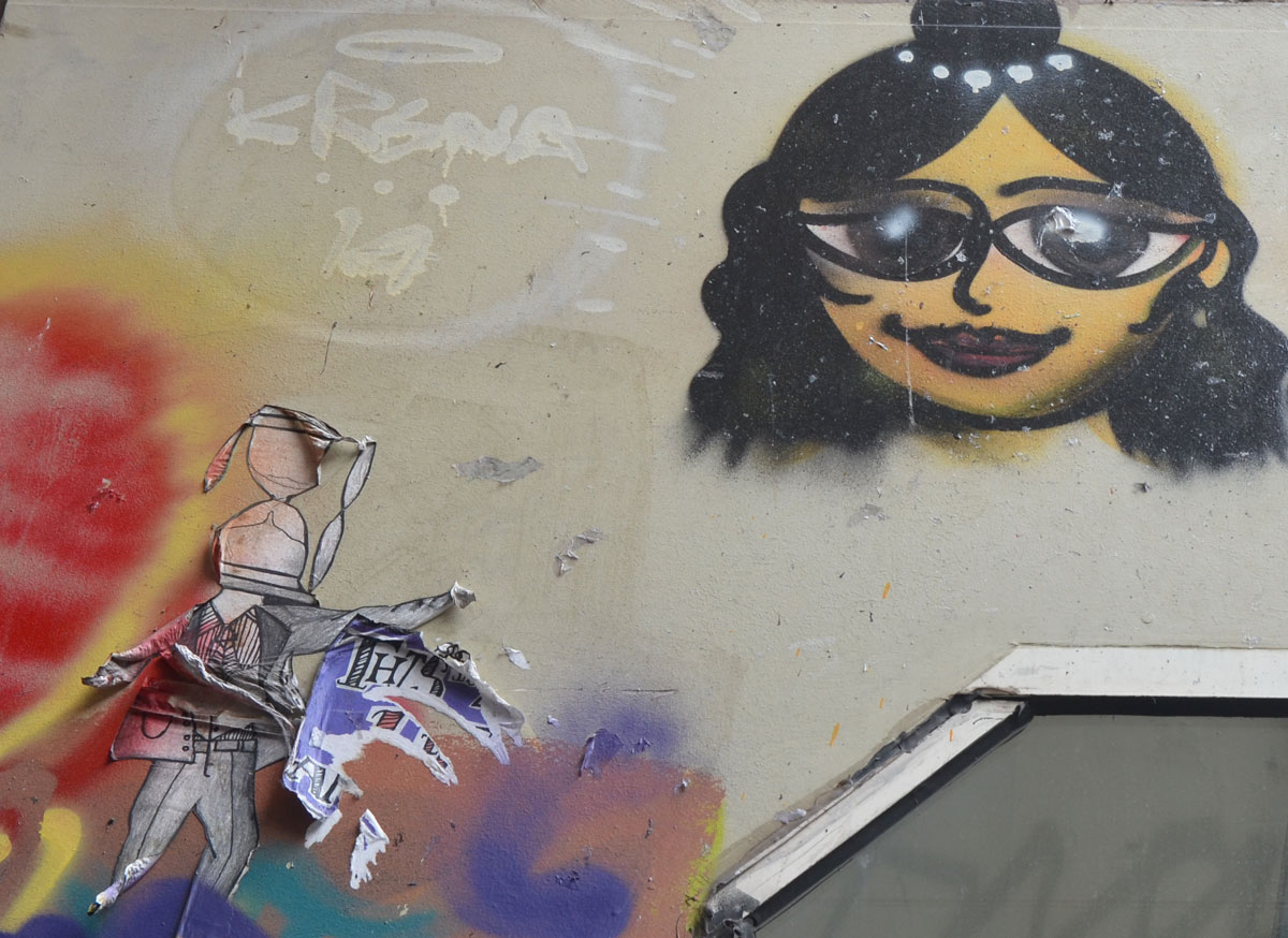 street art painting of a woman's head, shoulder length black hair, sunglasses and also a peeling paper wheatpaste