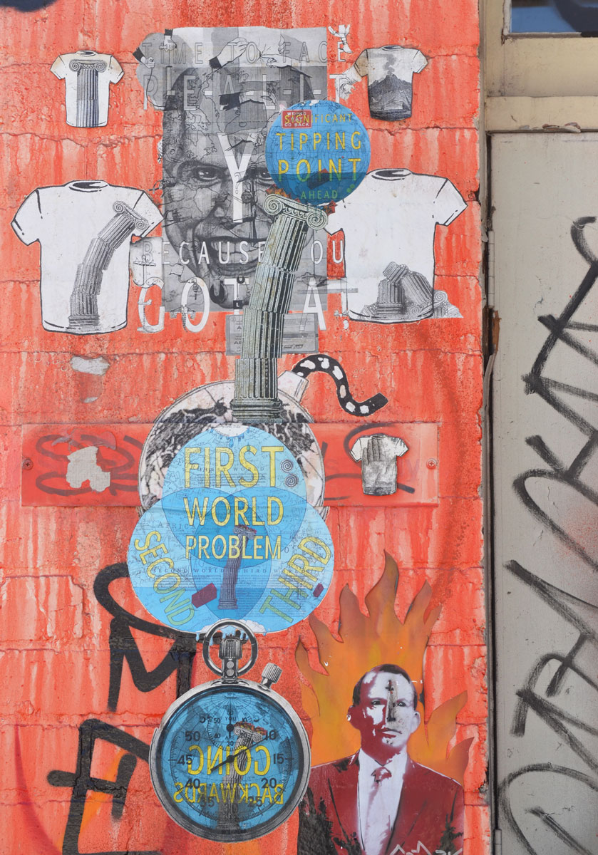 Many paste-ups on a part of a wall that has been painted orange. 