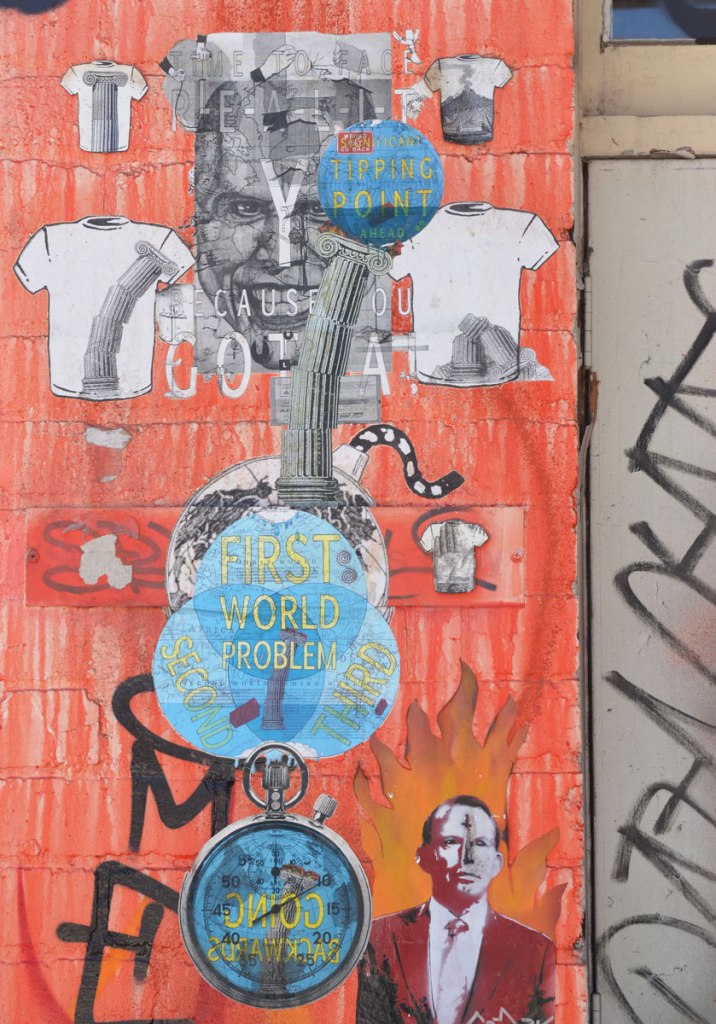 Many paste-ups on a part of a wall that has been painted orange.