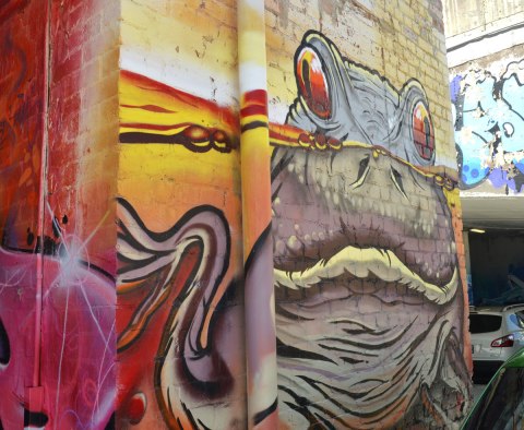 a street art painting of a frog partially submerged in water, his eyes are peaking out over the top of the water