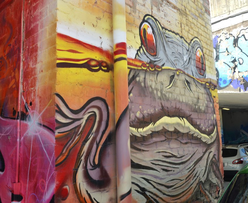 a street art painting of a frog partially submerged in water, his eyes are peaking out over the top of the water