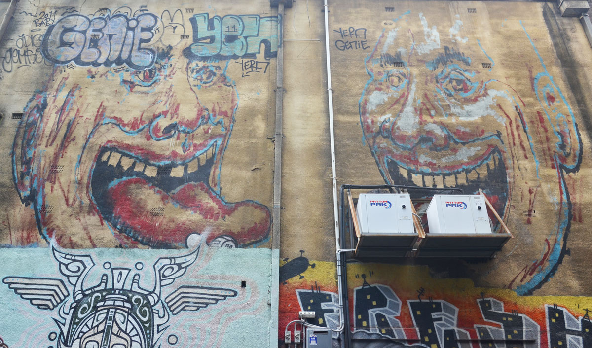 Two large faces painted high on a wall, the one on the left has a large tongue that is sticking out. Tagged Genie Yern, and yern genie.