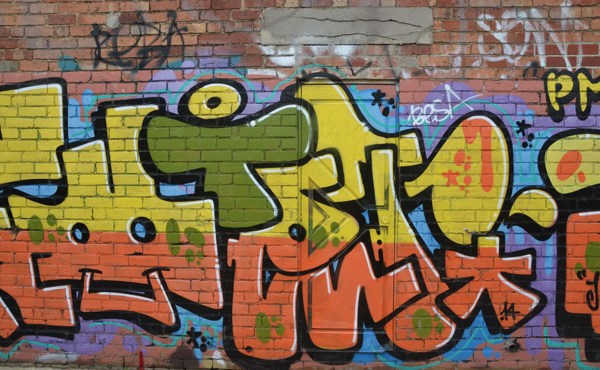 graffiti tag where the top half of the letters are yellow and the bottom half is orange. On green capital T is in the middle