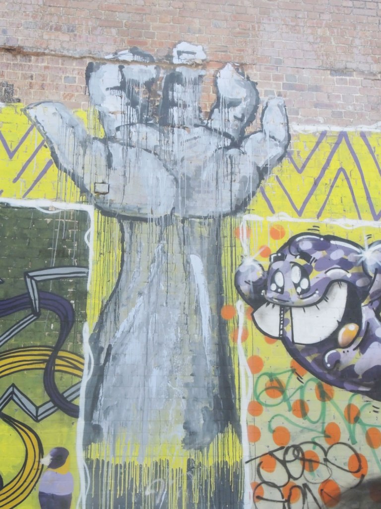 very large street art painting of an upstretched arm and open hand, in grey