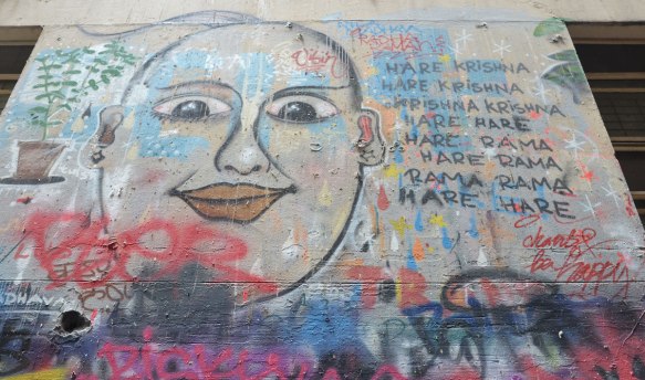 In Union Lane, Melbourne, on a wall, a drawing of buddha's face with the words to Hare Krishna written beside it, along with "be happy"