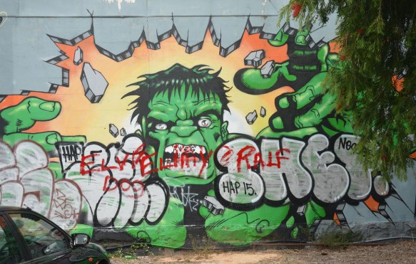 a street art painting of the Hulk (green man) smashing through a wall with just his hands. 