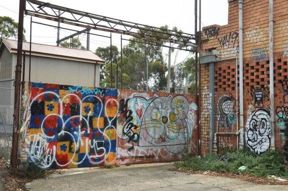 Outdoor graffiti on a corner wall by train tracks and a parking lot at Jewell train station