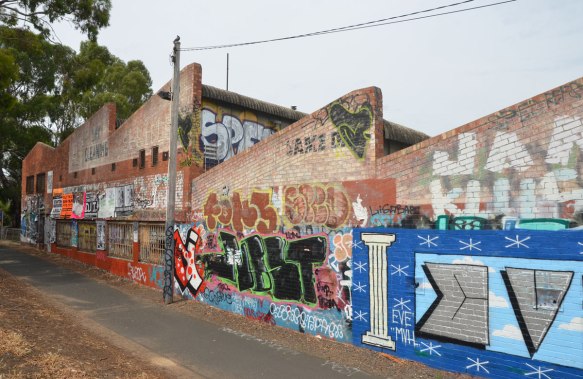 row of old brick buildings with diagonal rooflines covered with graffiti beside a bike path near Jewell train station