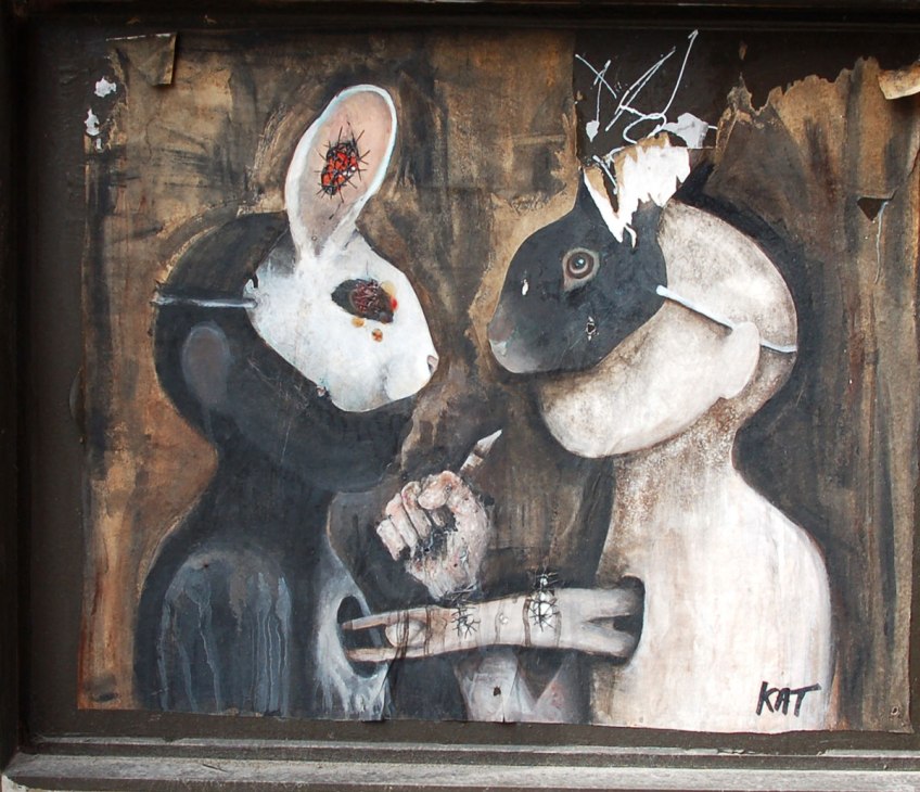 poster of anthromorphic creature with animal mask on - two rabbits, one black mask and one white mask, they are facing each other. A human figure is diving horizontally from a hole in the white creature (who is wearing the black mask) into a hole in the black creature