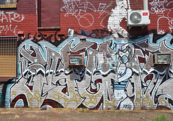 street art on a wall that includes a woman in a gas mask who is spray painting. 