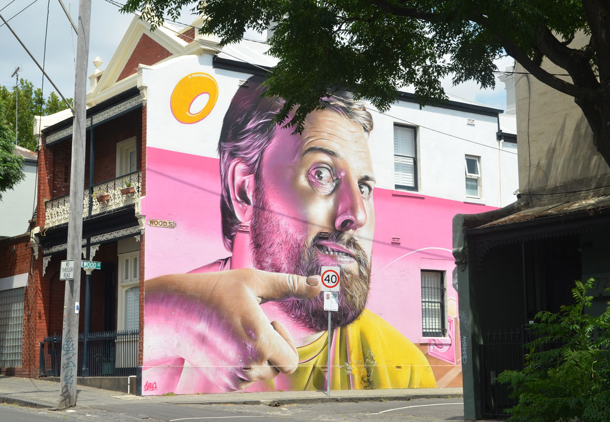 view of a street, houses with a mural on it, a man from the shoulders up