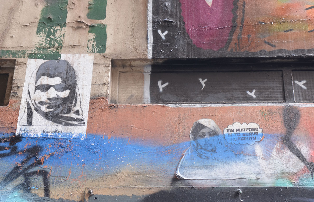 Two wheatpaste pictures of women. On the left is a woman in a head scarf with the name Malala Yousafai written below. On the right is another woman in a head scarf and a thought bubble that says 'My purpose is to serve humanity'.