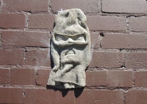 balaclava mounted on a brown brick wall, spray painted gray