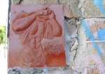 small relief sculpture graffiti of a headless man holding up his T-shirt while holding a camera. Great abs on the guy