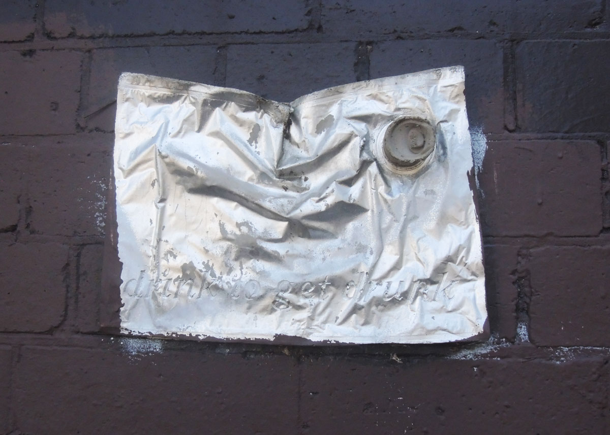 crumpled piece of metal with a small spout, looks like a metal gas container. Words written on it are "drink to get drunk"